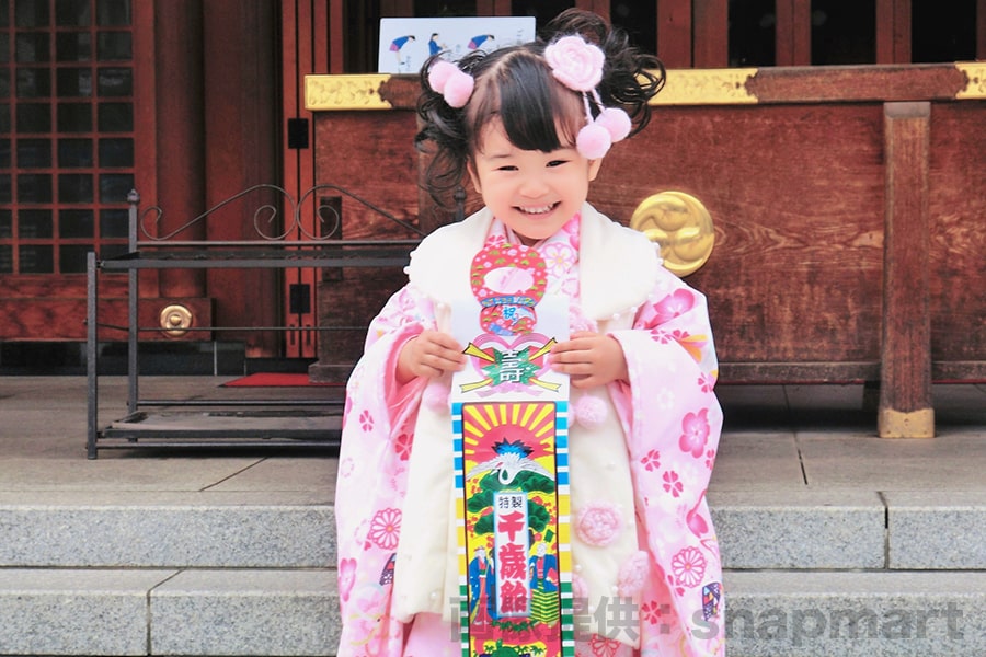 神社本殿前でかわいい表情で記念撮影する七五三三歳ちゃんの様子